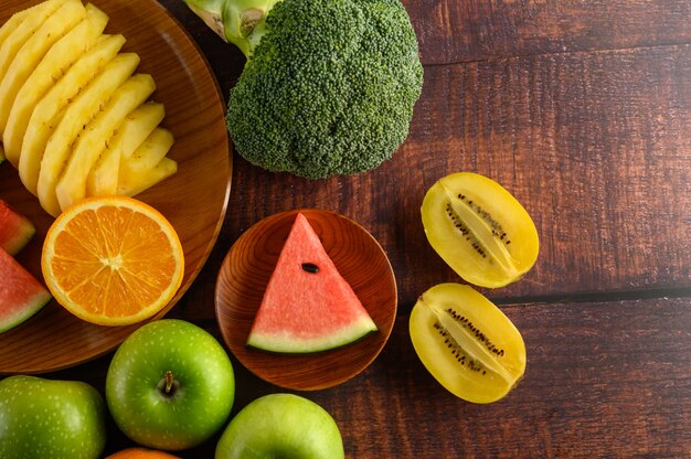 Sandía, naranja, piña, kiwi cortado en rodajas con manzanas y brócoli en un plato de madera y mesa de madera.