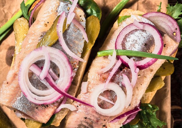 Sándwich abierto con pan, arenque en escabeche, pepino en escabeche y cebolla roja sobre un revestimiento de papel. Smorebrod danés, enfoque selectivo y espacio de copia