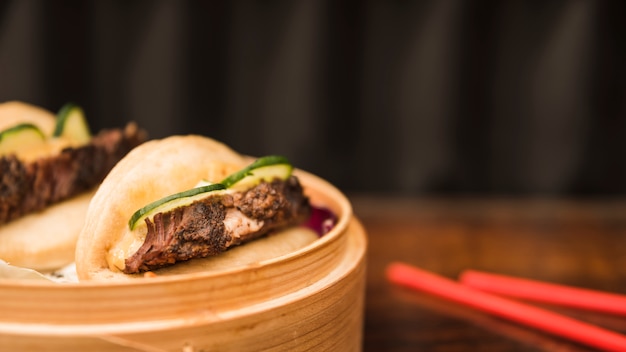 Sándwich al vapor de Bao Bun en cesta de vapor con palillos en mesa de madera