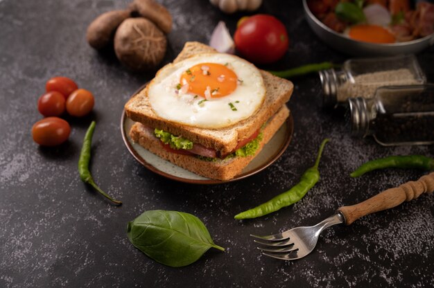 Sándwich de desayuno elaborado con pan, huevo frito, jamón y lechuga.