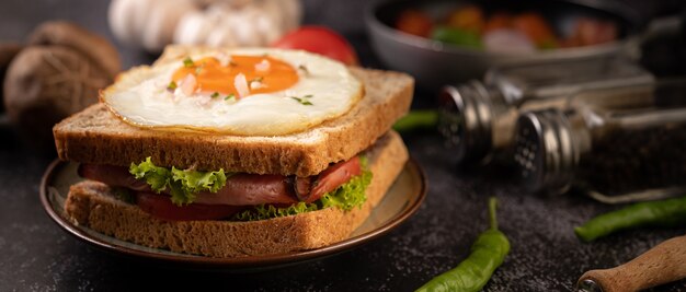 Sándwich de desayuno elaborado con pan, huevo frito, jamón y lechuga.