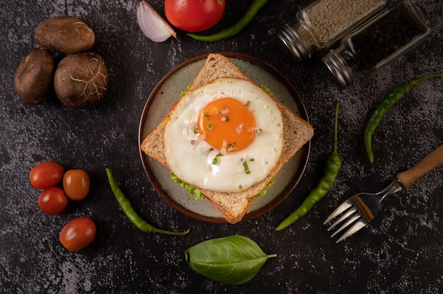 Sándwich de desayuno elaborado con pan, huevo frito, jamón y lechuga.