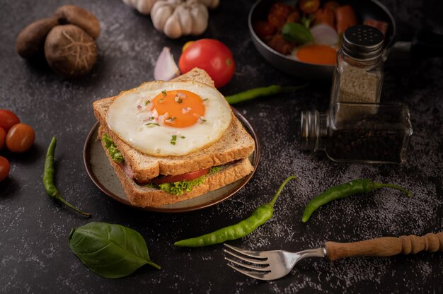 Sándwich de desayuno elaborado con pan, huevo frito, jamón y lechuga.