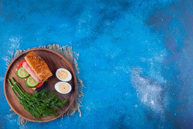 Sándwich, eneldo y huevo en rodajas a bordo en azul.