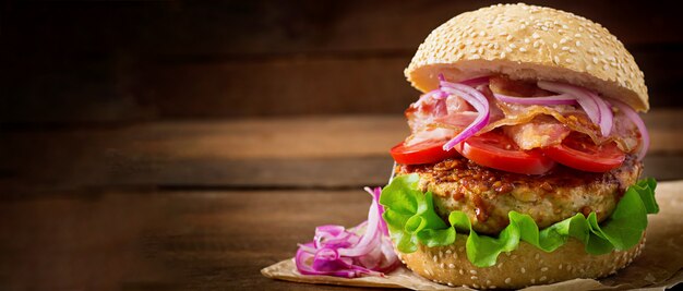 Sándwich grande - hamburguesa con carne de res, cebolla roja, tomate y tocino frito.