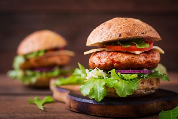 Sándwich grande - hamburguesa con jugosa hamburguesa de pollo, queso, tomate y cebolla roja en mesa de madera