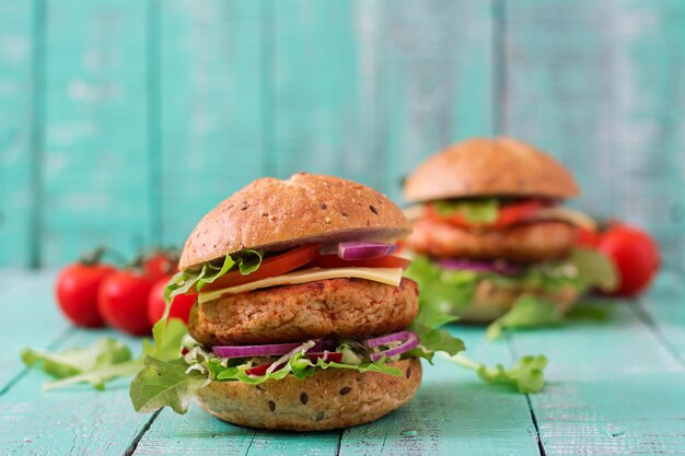 Sándwich grande - hamburguesa con jugosa hamburguesa de pollo, queso, tomate y cebolla roja en mesa de madera