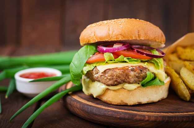 Sándwich grande - hamburguesa con jugosa hamburguesa de ternera, queso, tomate y cebolla roja en mesa de madera