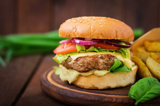 Sándwich grande - hamburguesa con jugosa hamburguesa de ternera, queso, tomate y cebolla roja en mesa de madera