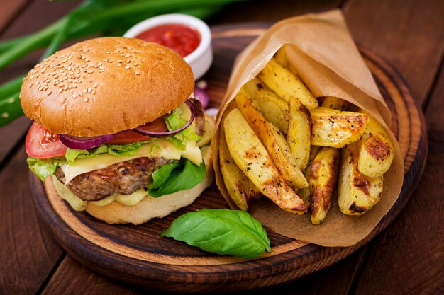 Sándwich grande - hamburguesa con jugosa hamburguesa de ternera, queso, tomate y cebolla roja en mesa de madera