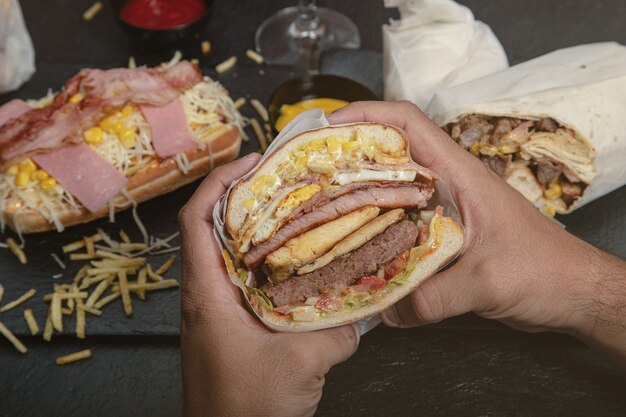 Sándwich grande con varios tipos de carne y maíz y algunas hamburguesas alrededor.