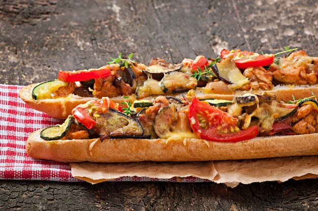 Sándwich grande con verduras asadas (calabacín, berenjenas, tomates) con queso y tomillo sobre fondo de madera vieja