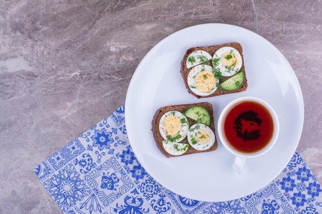 Sándwich de huevo cocido con una taza de té en un plato blanco.