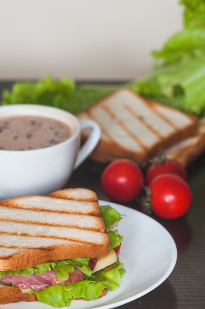 Sándwich con jamón; Hoja de espinaca y queso en plato blanco con café