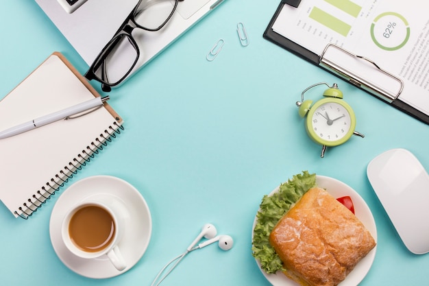 Sandwich, laptop, lentes, reloj despertador, mouse, auriculares sobre fondo azul