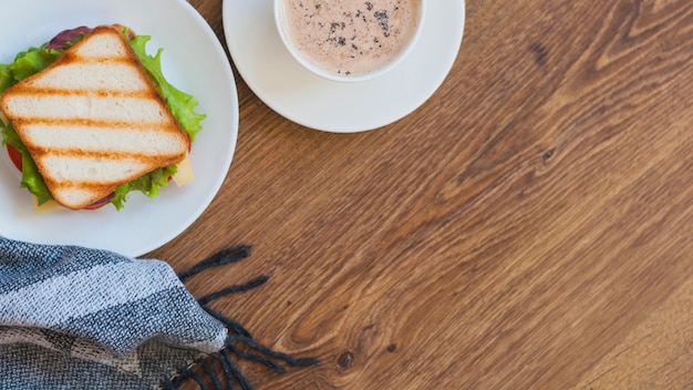 Sándwich a la parrilla y una taza de café en la mesa de madera