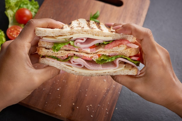 Foto gratuita sándwich a la plancha con jamón, queso, tomate y lechuga servido sobre tabla de cortar de madera.