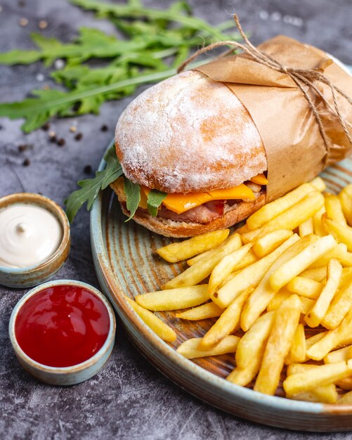 Sandwich de pollo con queso cheddar y rúcula servido con papas fritas, mayonesa y ketchup