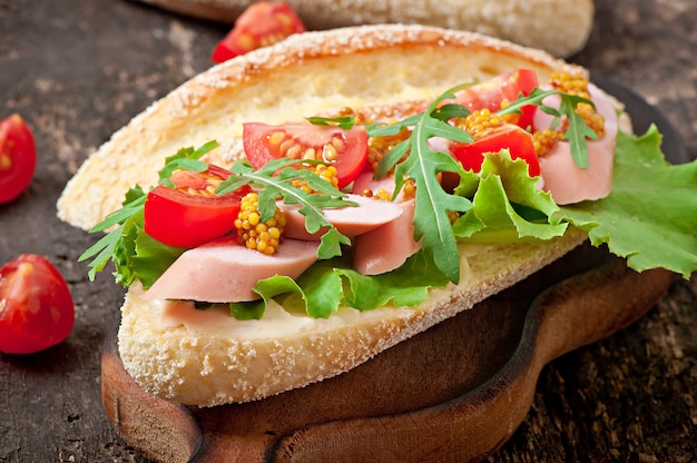 Sandwich con salchichas, lechuga, tomate y rúcula en la superficie de madera vieja