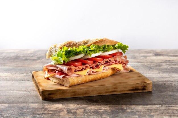 Sándwich submarino con jamón, queso, lechuga, tomate, cebolla, mortadela y salchicha en mesa de madera