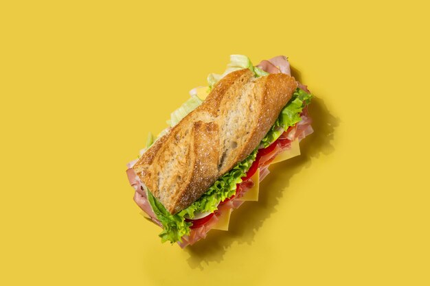 Sándwich submarino con jamón, queso, lechuga, tomate, cebolla, mortadela y salchicha sobre fondo amarillo