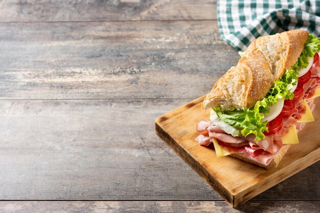 Sándwich submarino con jamón, queso, lechuga, tomate, cebolla, mortadela y salchicha sobre mesa de madera