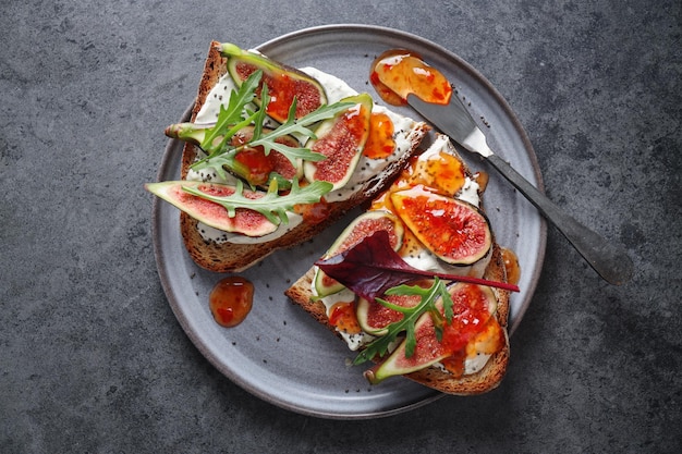 Sándwich de tostadas con higos sobre queso crema con mermelada servido en plato