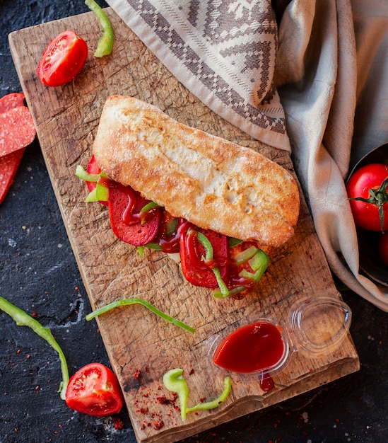 Sándwich turco suk ekmek en baguette sobre una mesa de madera con mantel y verduras alrededor