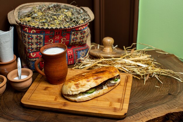 Un sándwich de vista frontal de cerca llamado doner con carne y verduras en rodajas en el interior junto con yogur en la superficie de madera marrón