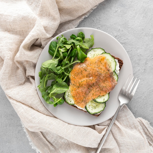 Sándwich de vista superior con pepinos y salmón en un plato con espinacas y tenedor