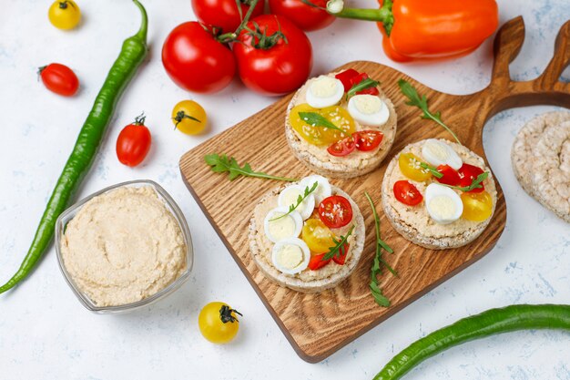 Sándwiches abiertos de pasteles de arroz con hummus, verduras y huevo de codorniz, desayuno o almuerzo saludable.