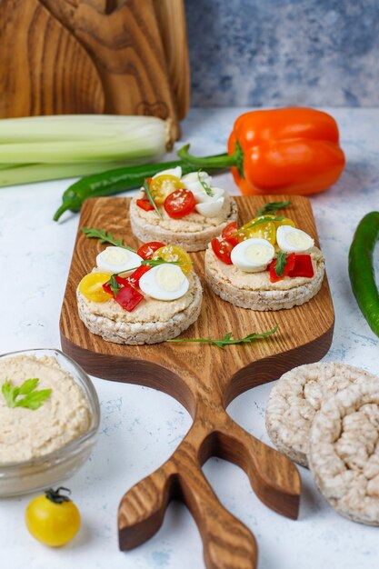 Sándwiches abiertos de pasteles de arroz con hummus, verduras y huevo de codorniz, desayuno o almuerzo saludable.