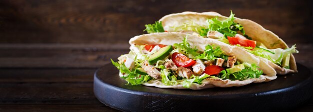 Sandwiches de pan de pita con carne de pollo a la parrilla, aguacate, tomate, pepino y lechuga servidos en una mesa de madera