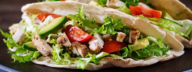 Sandwiches de pan de pita con carne de pollo a la parrilla, aguacate, tomate, pepino y lechuga servidos en una mesa de madera