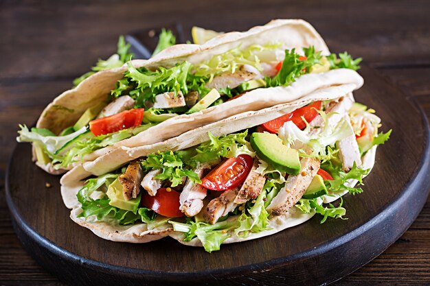 Sandwiches de pan de pita con carne de pollo a la parrilla, aguacate, tomate, pepino y lechuga servidos en una mesa de madera