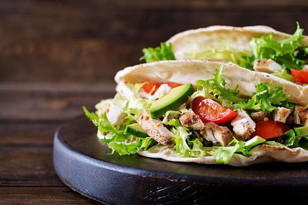 Sandwiches de pan de pita con carne de pollo a la parrilla, aguacate, tomate, pepino y lechuga servidos en una mesa de madera