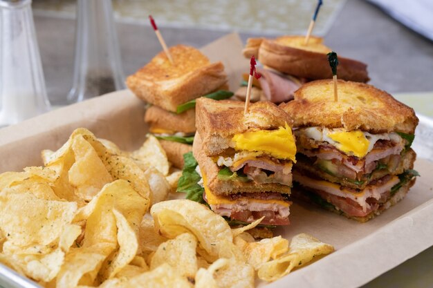 Sándwiches rellenos de jamón de lechuga y queso junto a patatas fritas en un recipiente