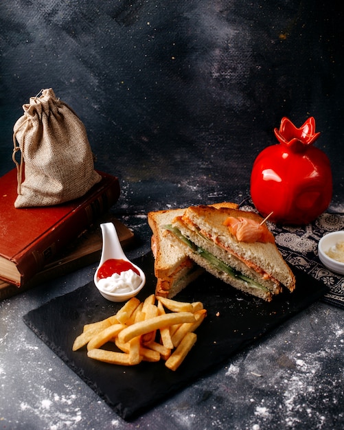 Sándwiches de vista frontal en rodajas junto con papas fritas en el escritorio negro y piso gris