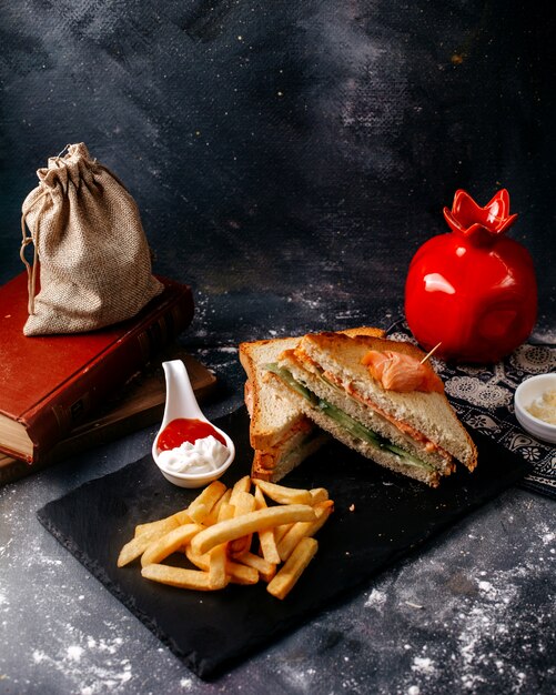 Sándwiches de vista frontal en rodajas junto con papas fritas en el escritorio negro y piso gris