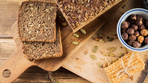 Sano pan de semillas de girasol y tazón de avellanas con barra de proteína en una tabla de cortar