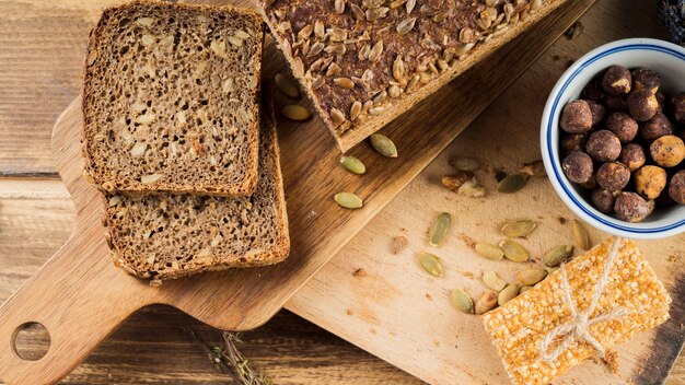 Sano pan de semillas de girasol y tazón de avellanas con barra de proteína en una tabla de cortar