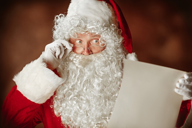 Santa Claus con una lujosa barba blanca, un gorro de Papá Noel y un traje rojo leyendo una carta