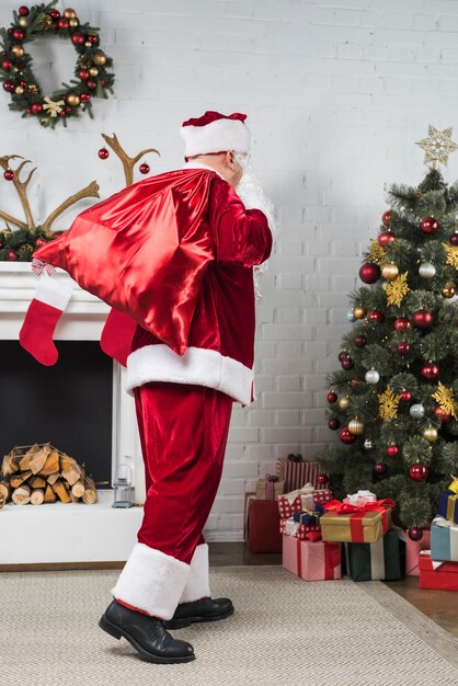Santa con gran saco de regalos a espaldas va al árbol de navidad