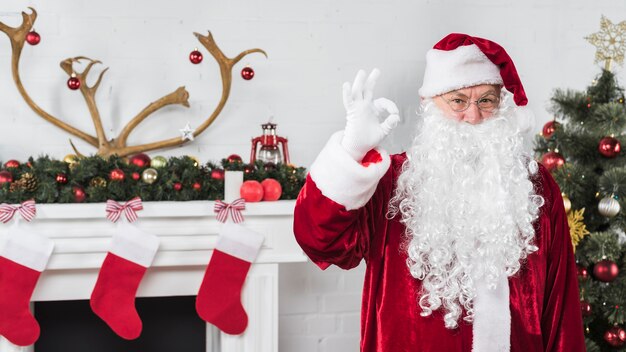 Santa que muestra gesto aceptable junto a la chimenea