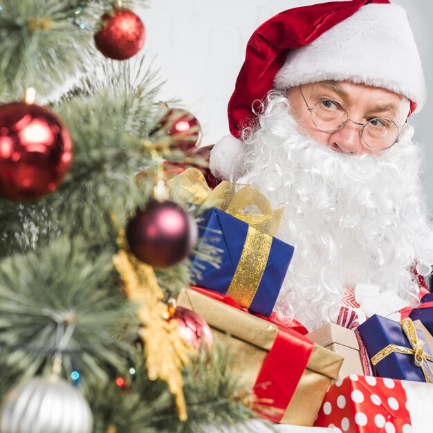 Santa con regalos en manos cerca de arbol de navidad