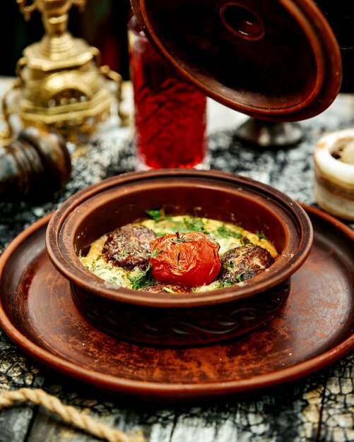 Una sartén de cerámica con albóndigas de carne cocidas en huevo con espinacas cubiertas con tomate