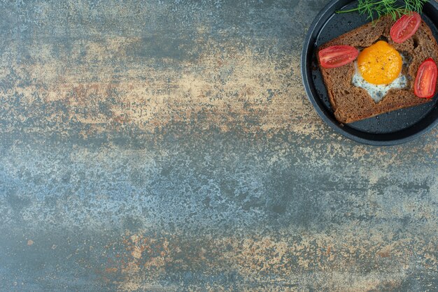 Una sartén oscura con huevo frito y tomate sobre fondo de mármol