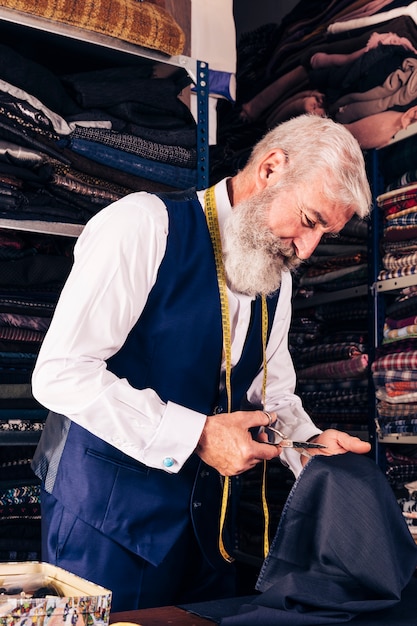 Sastre masculino mayor que corta el pedazo de paño en la tabla en su tienda