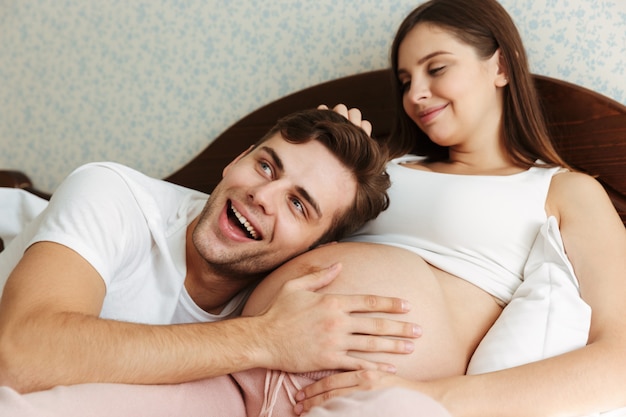 Satisfecha joven esposa embarazada acostada en la cama con su esposo