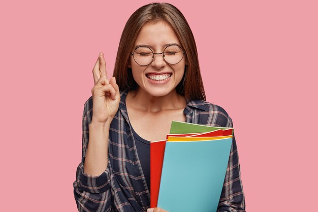 Satisfecho joven empresaria posando contra la pared rosa con gafas